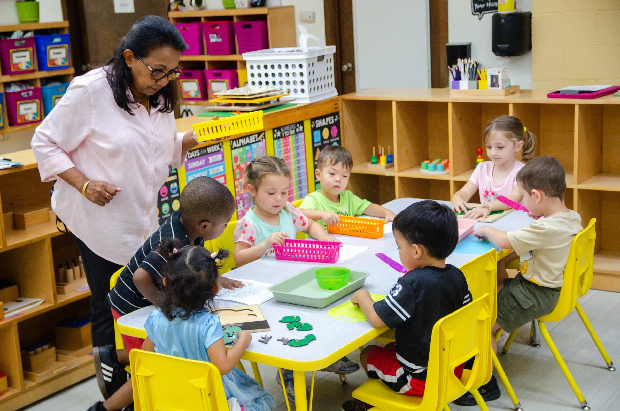 A teacher walks around a table of children working together on an activity.