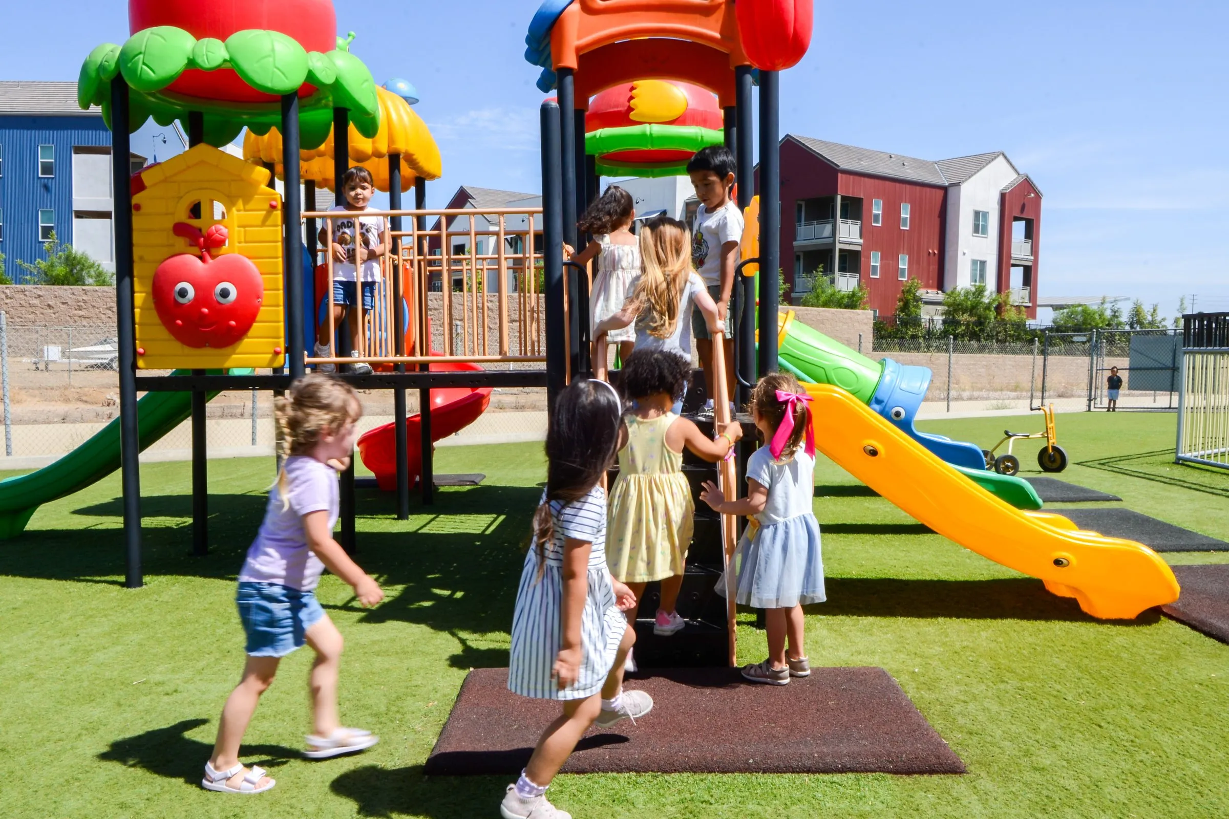 Children climb and play on the colorful play structure on the turf playground.